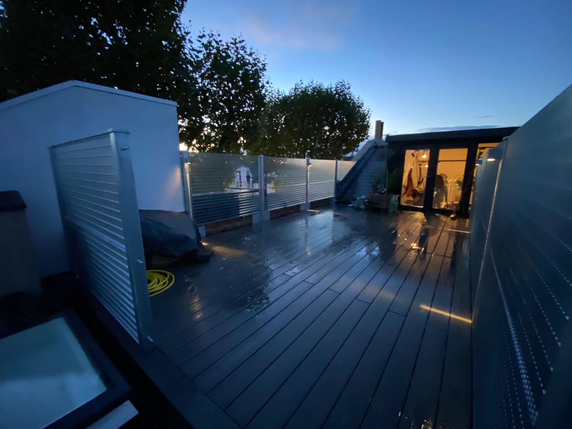 Rear deck at dusk — composite boards, a glass balustrade and a lit garden room beyond