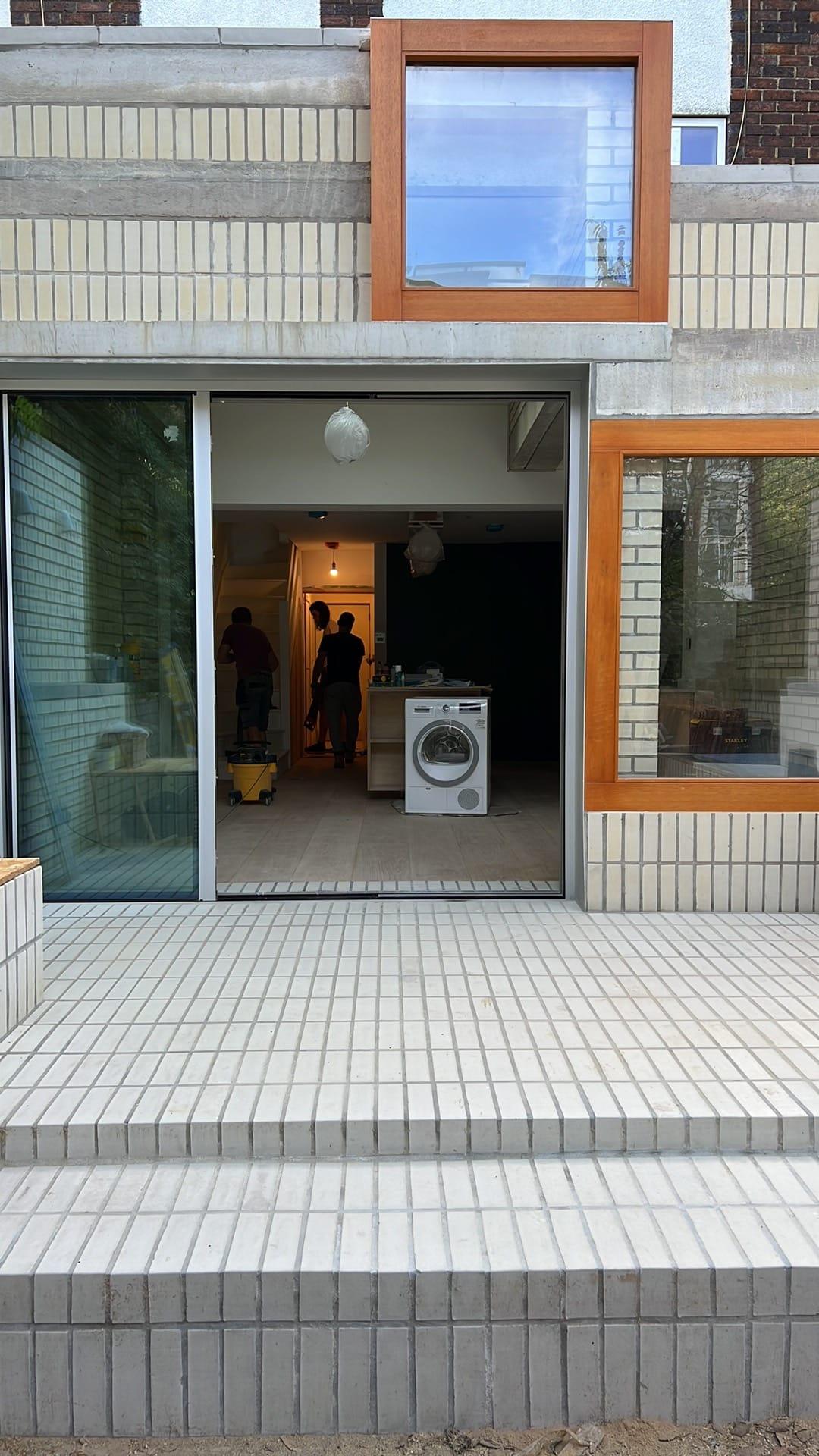 Rear elevation in glazed white brick — sliding doors at garden level and a timber-framed window above