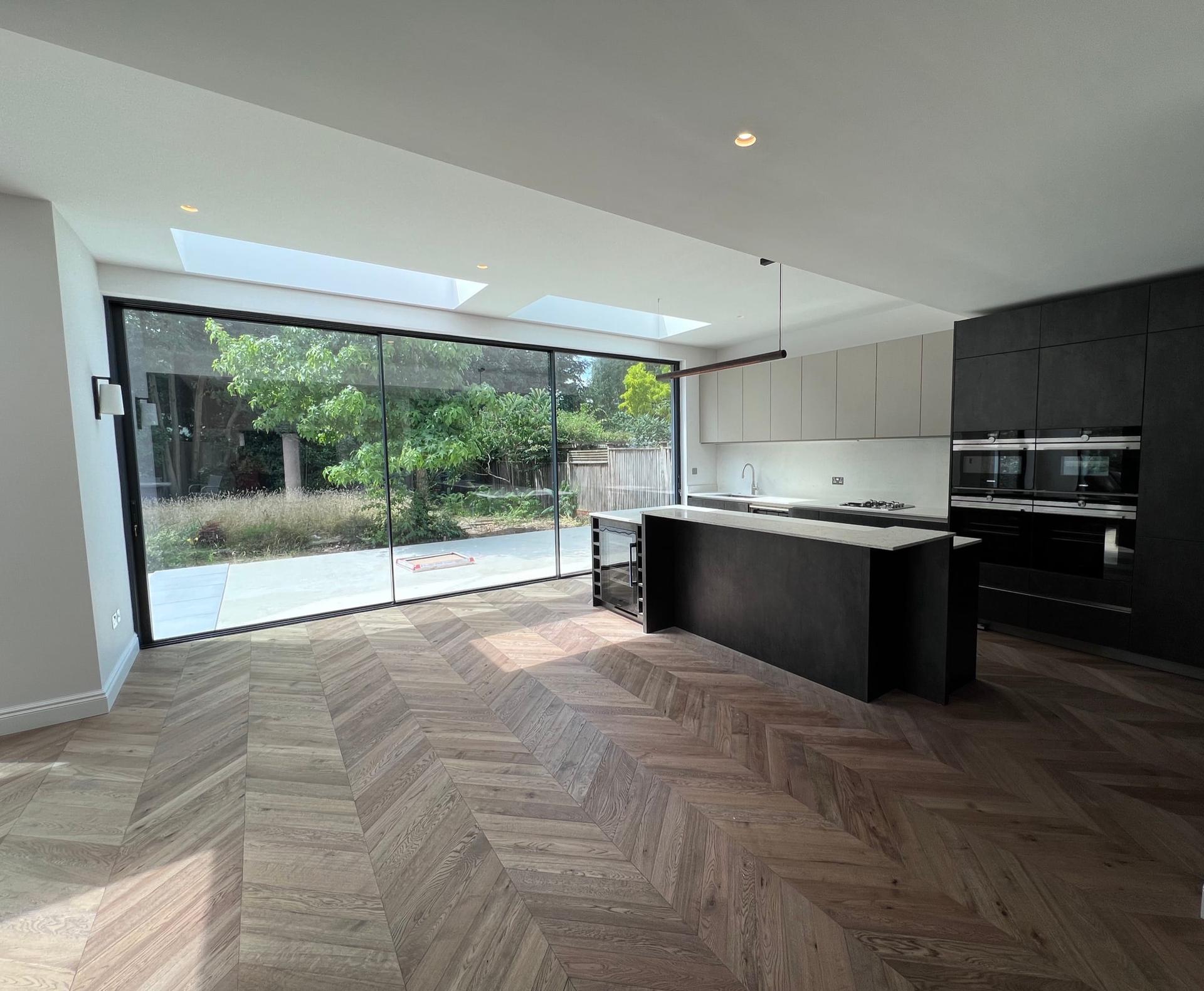 Open-plan kitchen and dining room in a rear extension, with rooflights, a dark island and chevron oak flooring