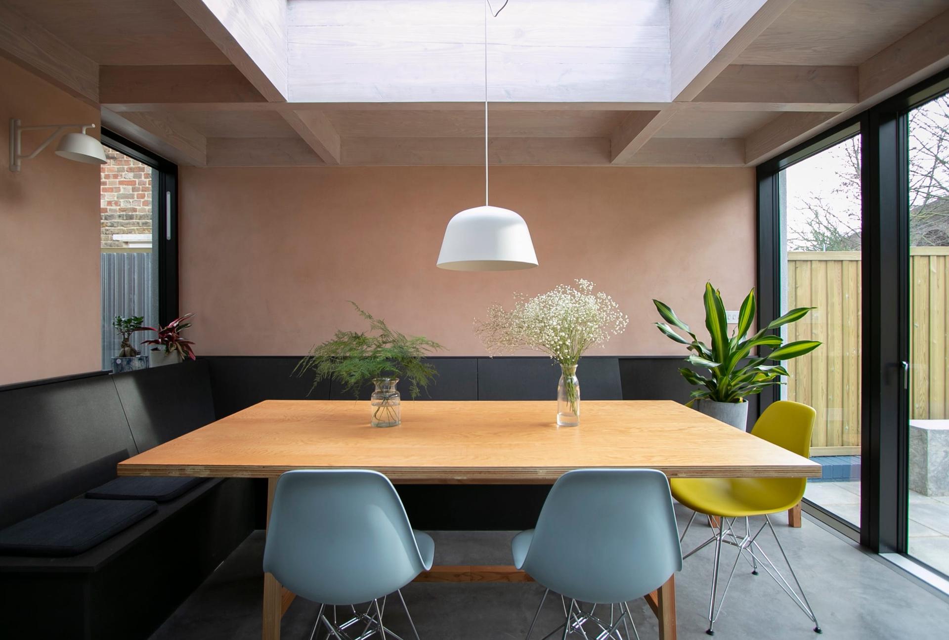Dining area in a rear extension — pink plaster walls, a fitted banquette, a rooflight and polished concrete underfoot