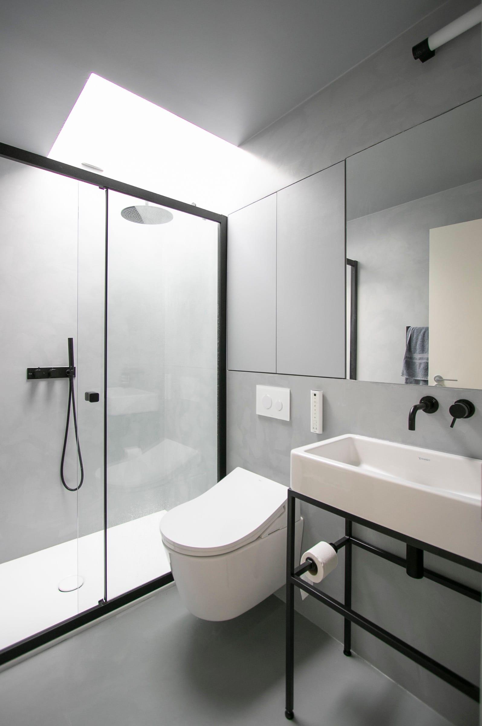 Microcement shower room with a black rain shower, a wall-hung basin on a steel frame and a rooflight over