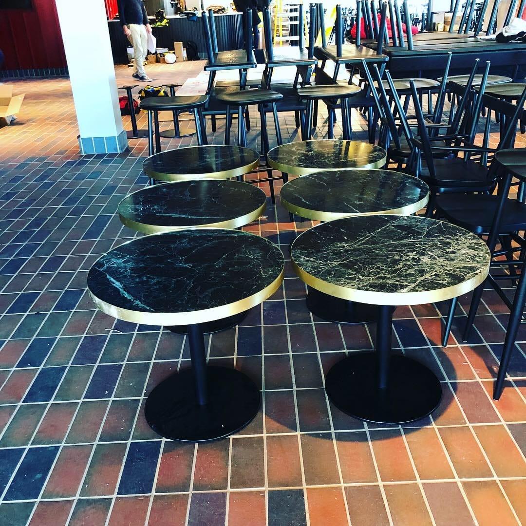 Cafe fit-out — green marble bistro tables with brass edging on a terracotta tiled floor
