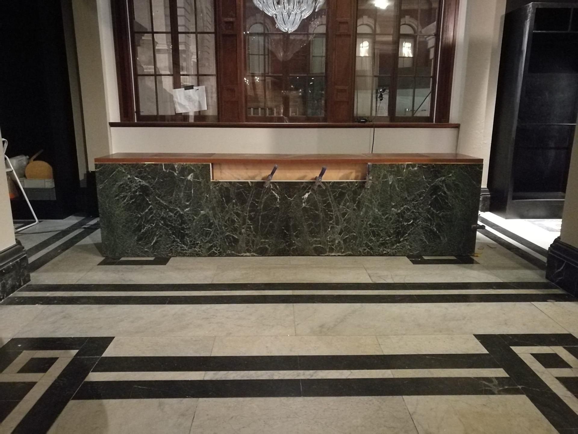 Green marble reception counter with a timber shelf, set on a patterned stone floor