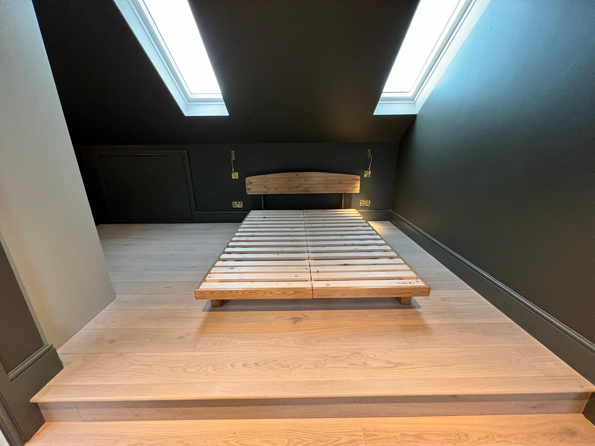 Loft bedroom in dark green with an oak platform bed base and a rooflight in the slope