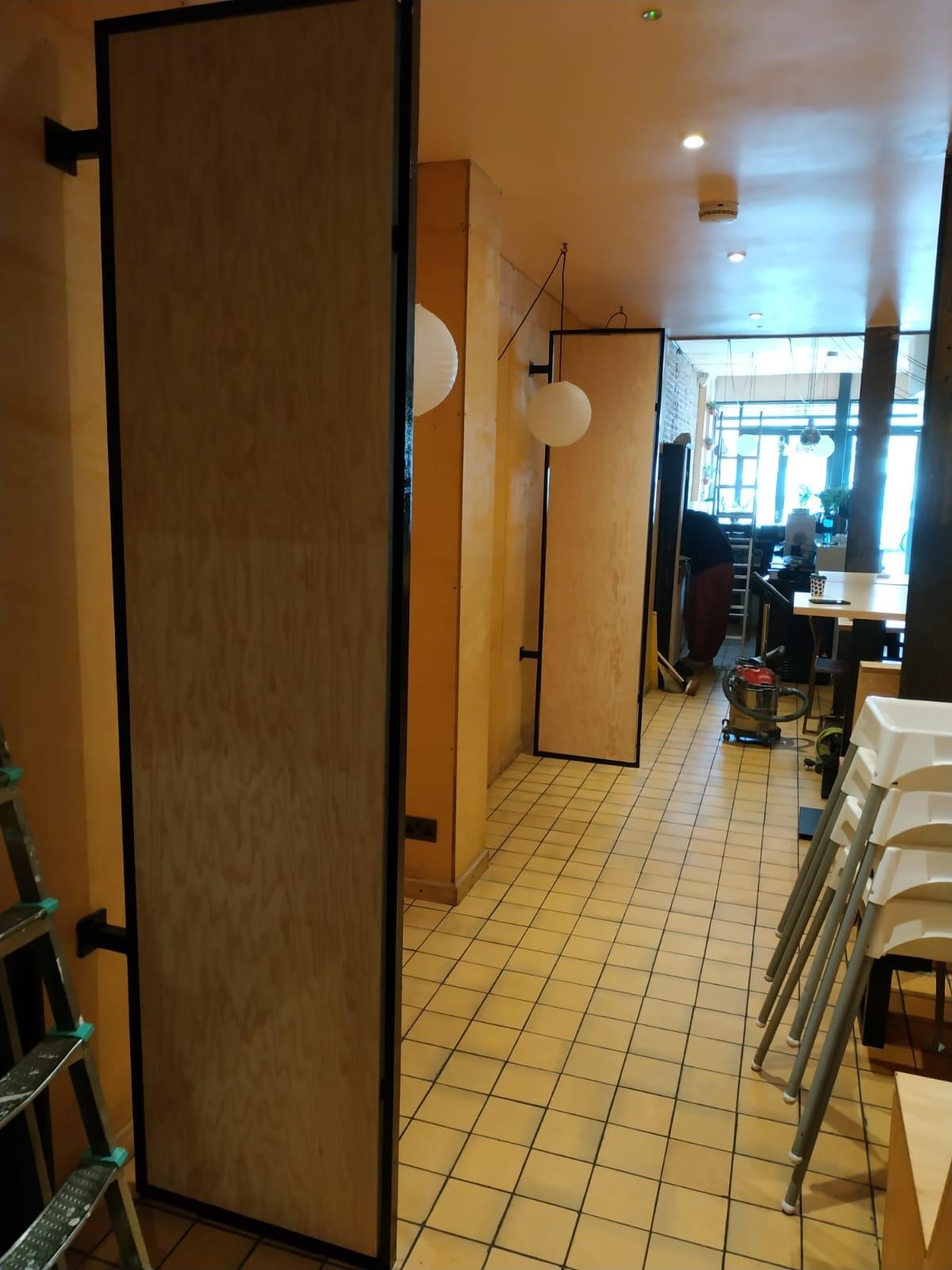 Cafe mid fit-out — plywood partitions in steel frames over a yellow tiled floor