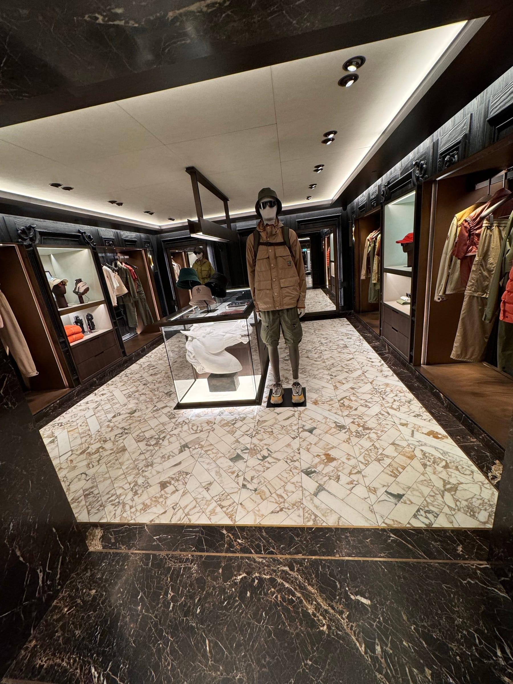 Retail shopfloor with a marble floor inlay, lit display cabinetry and a central mannequin plinth