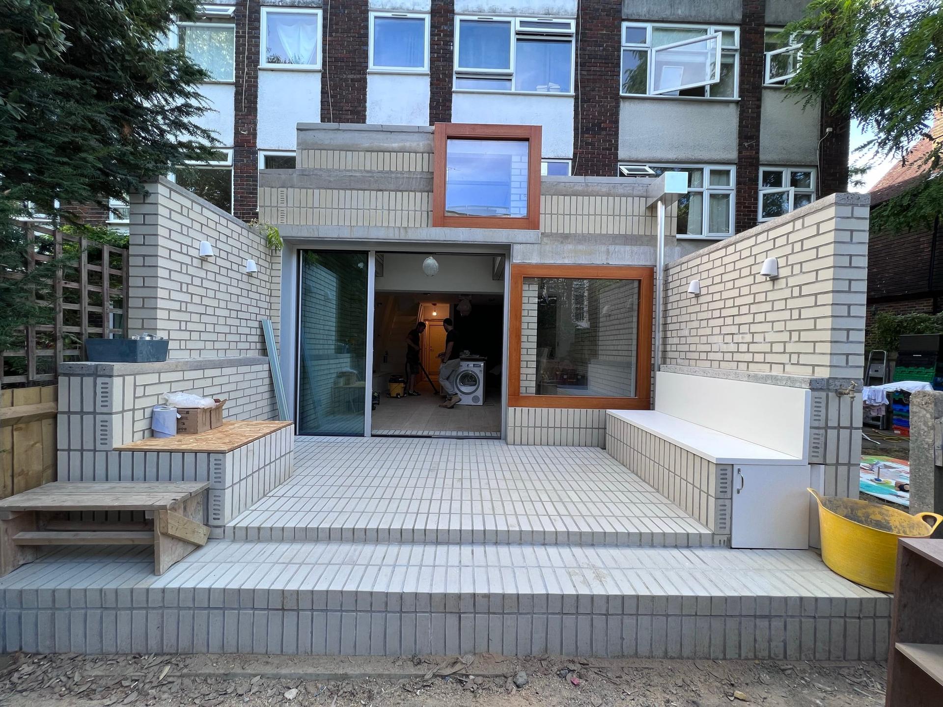 Rear elevation in glazed white brick with a raised terrace, brick steps and a built-in timber bench