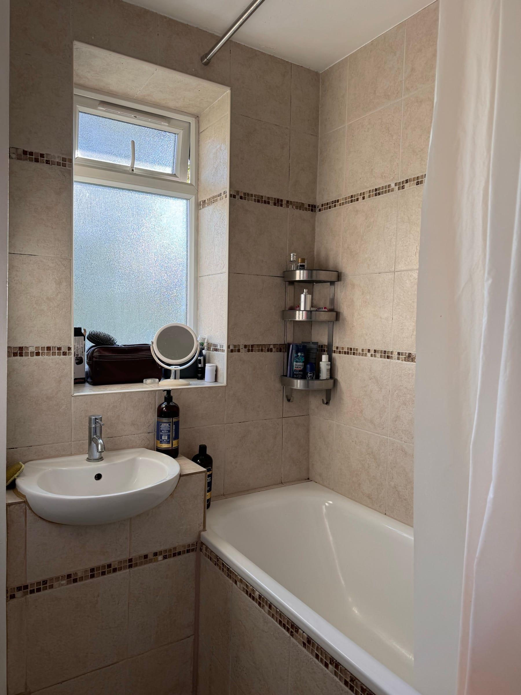 Family bathroom with a shower over the bath, beige wall tiling and a mosaic border