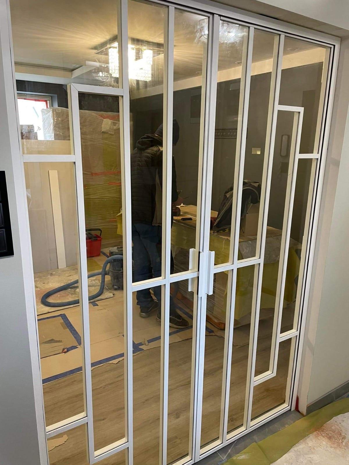 White steel-framed glazed screen being installed between two rooms