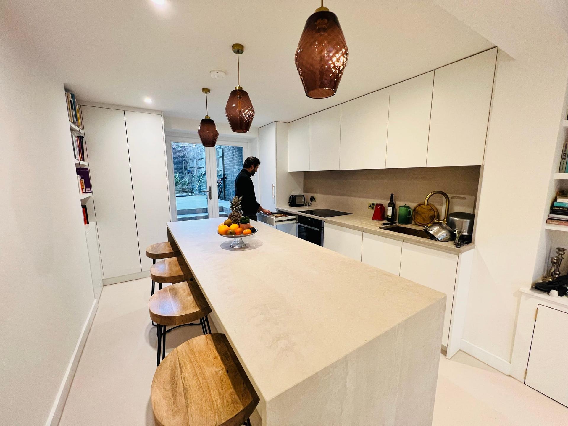 Galley kitchen with a travertine island and breakfast bar, copper pendants and full-height shelving