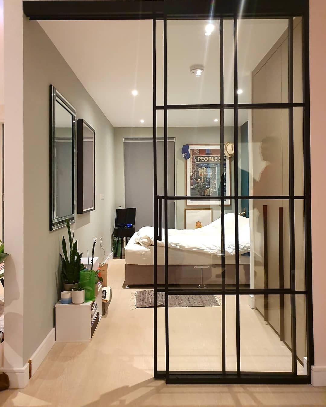 Black steel glazed screen dividing a hallway from a bedroom, with a pocket door in the frame