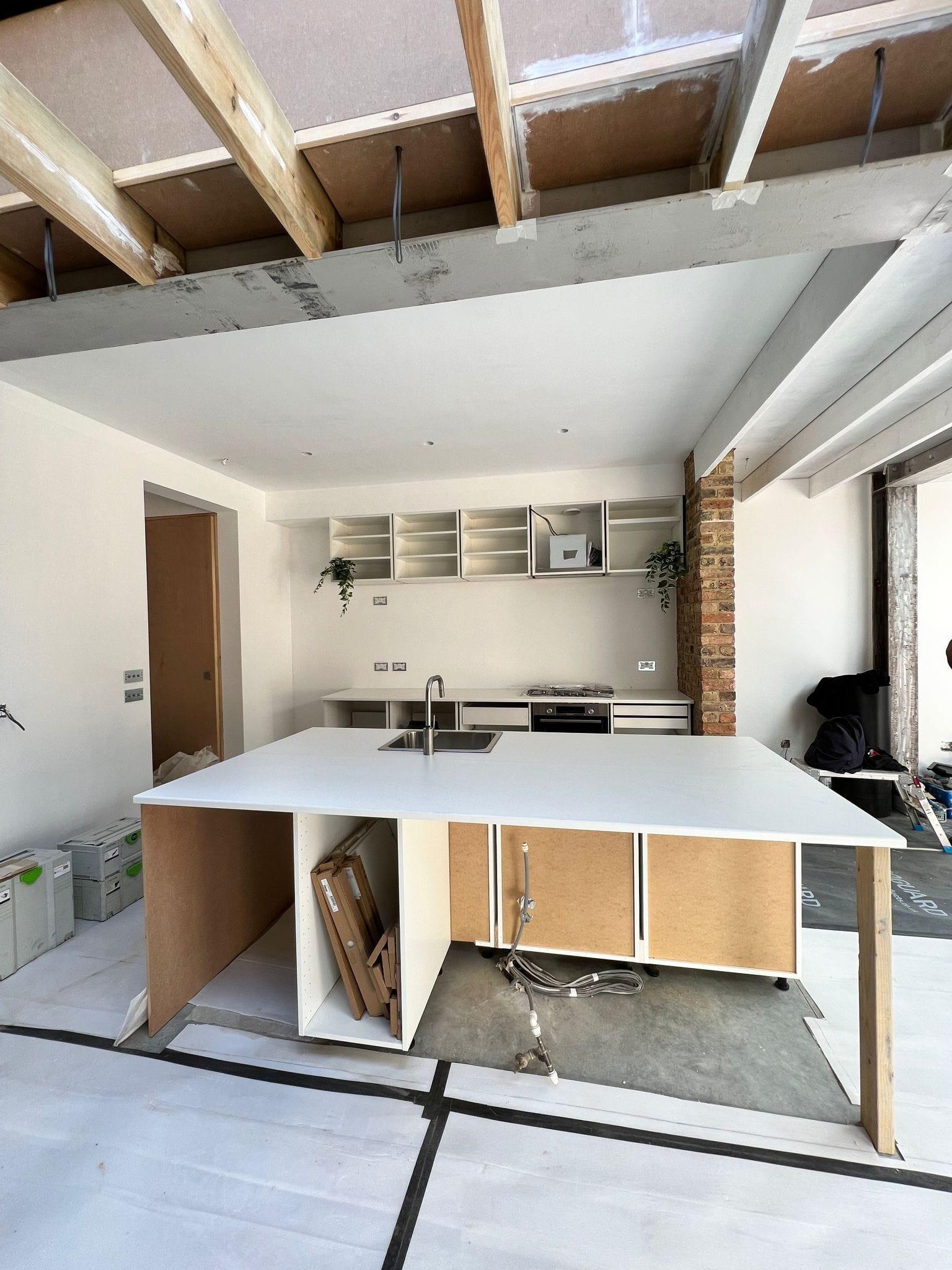 Kitchen island going in beneath exposed timber joists, with a brick return and open shelving behind