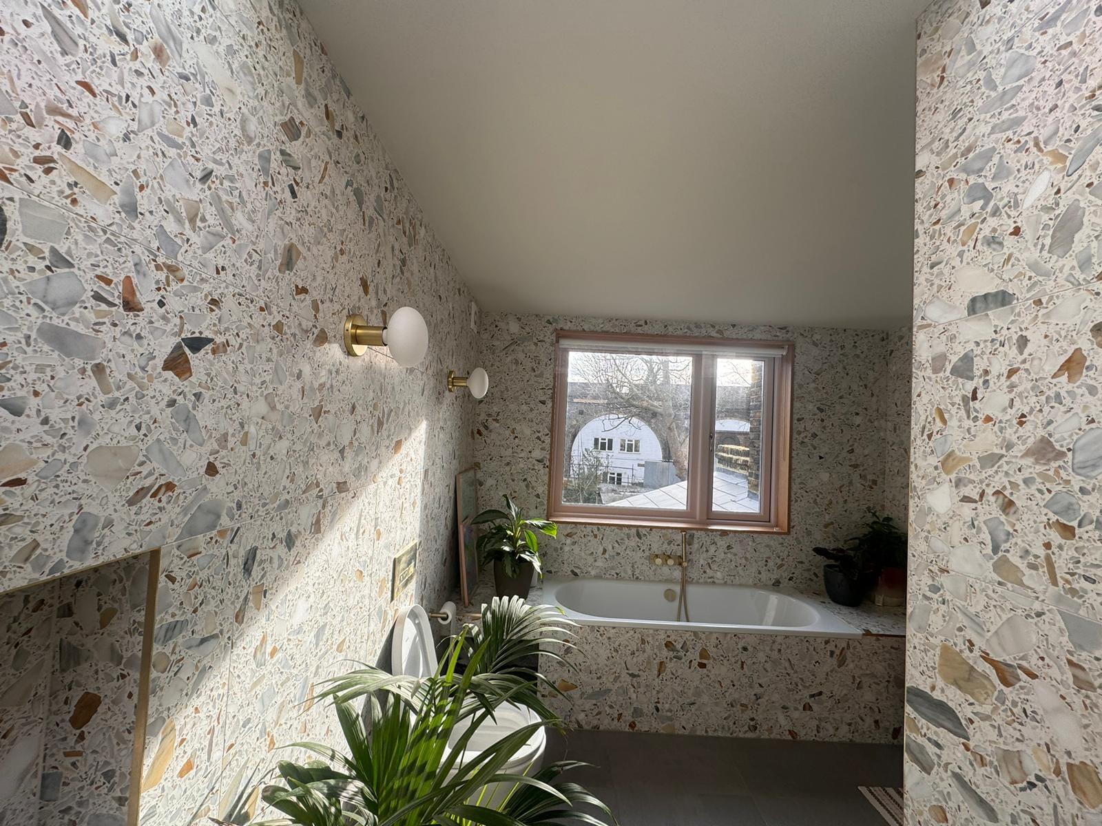 Bathroom clad floor to ceiling in terrazzo, including the bath surround, with a timber-framed window
