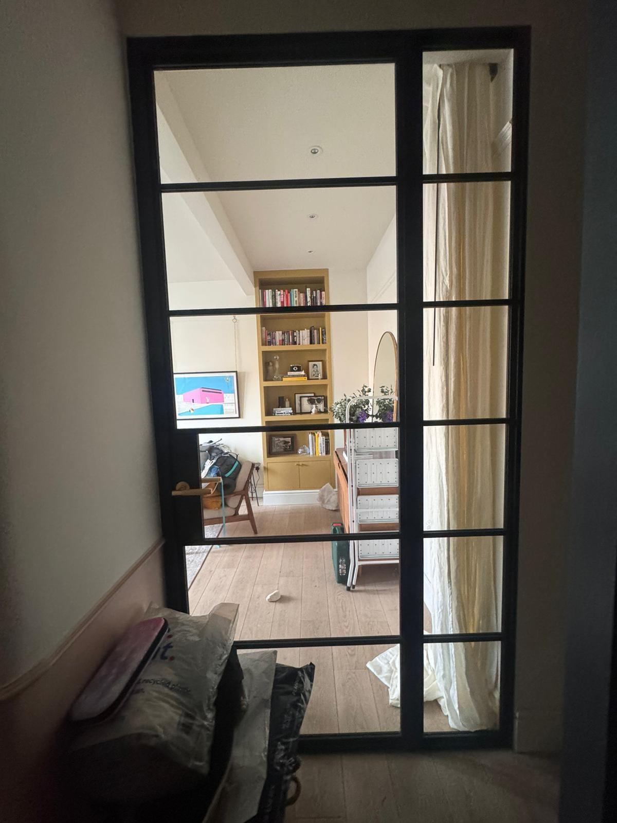 Black steel-framed glazed door from a hallway into a living room