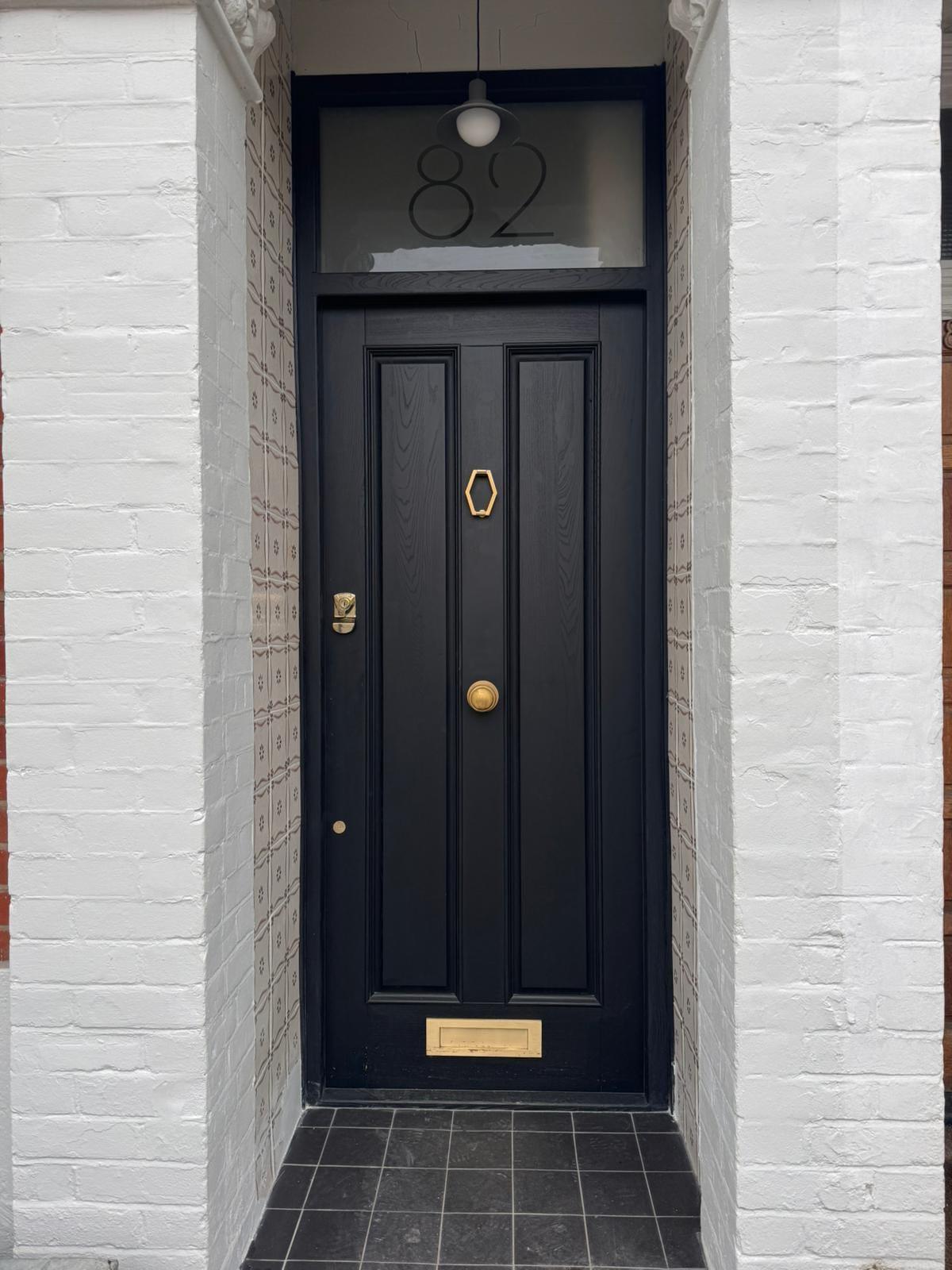 Navy panelled front door with a brass letterplate, in a white-painted brick porch over black tiles