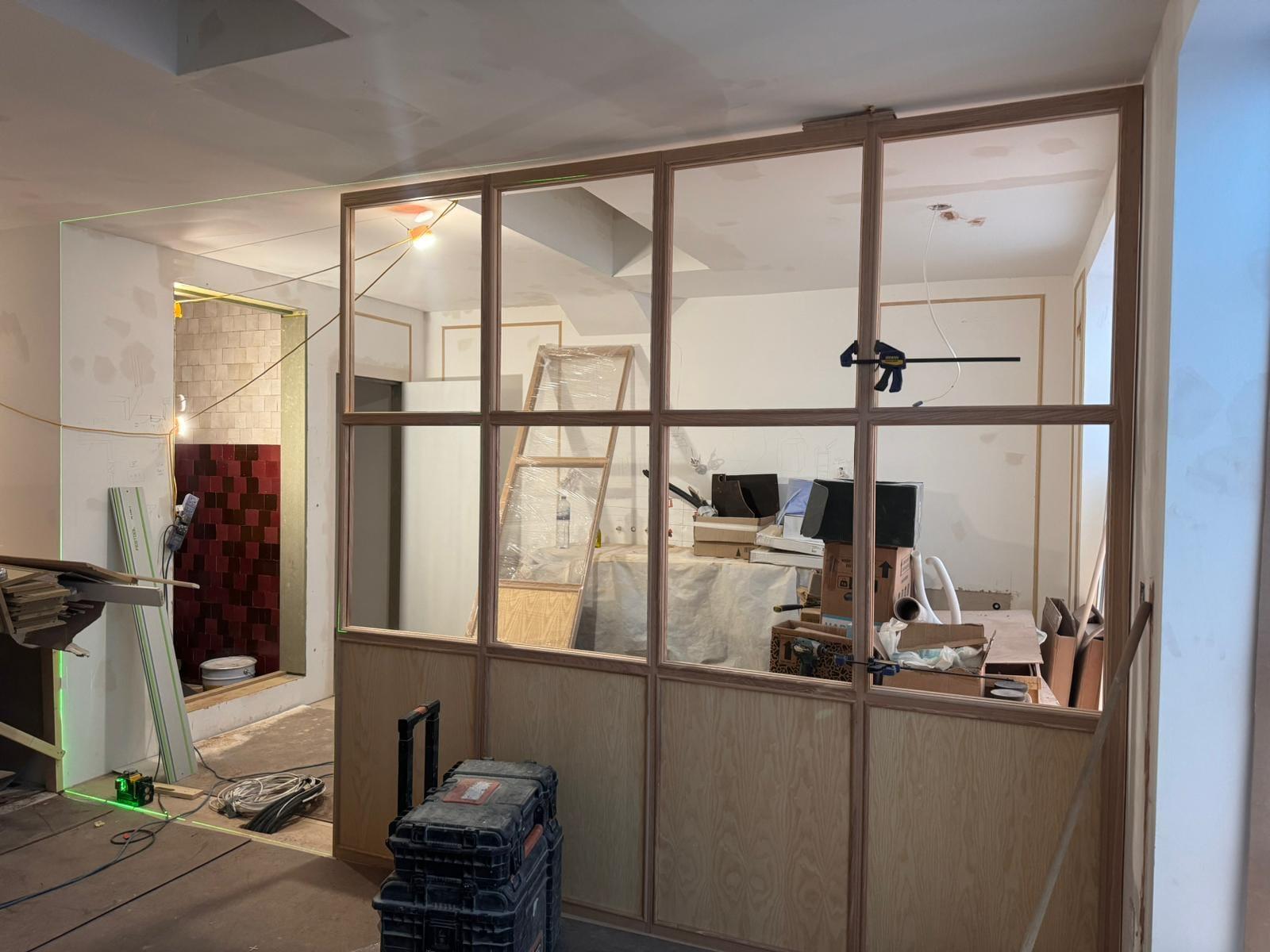 Oak-framed glazed partition being installed on site, the floor still sheeted