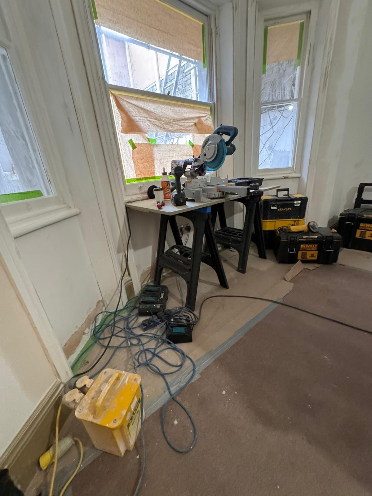 Mitre saw set up on trestles in a bay window, the room sheeted for second fix