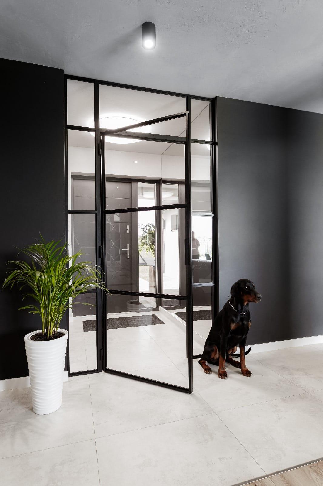 Black steel pivot doors between an entrance hall and a living room