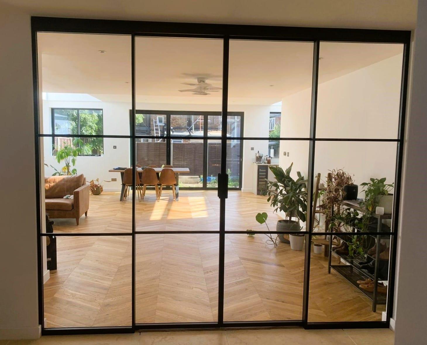 Full-width black Crittall-style screen dividing a living room from the kitchen and garden beyond