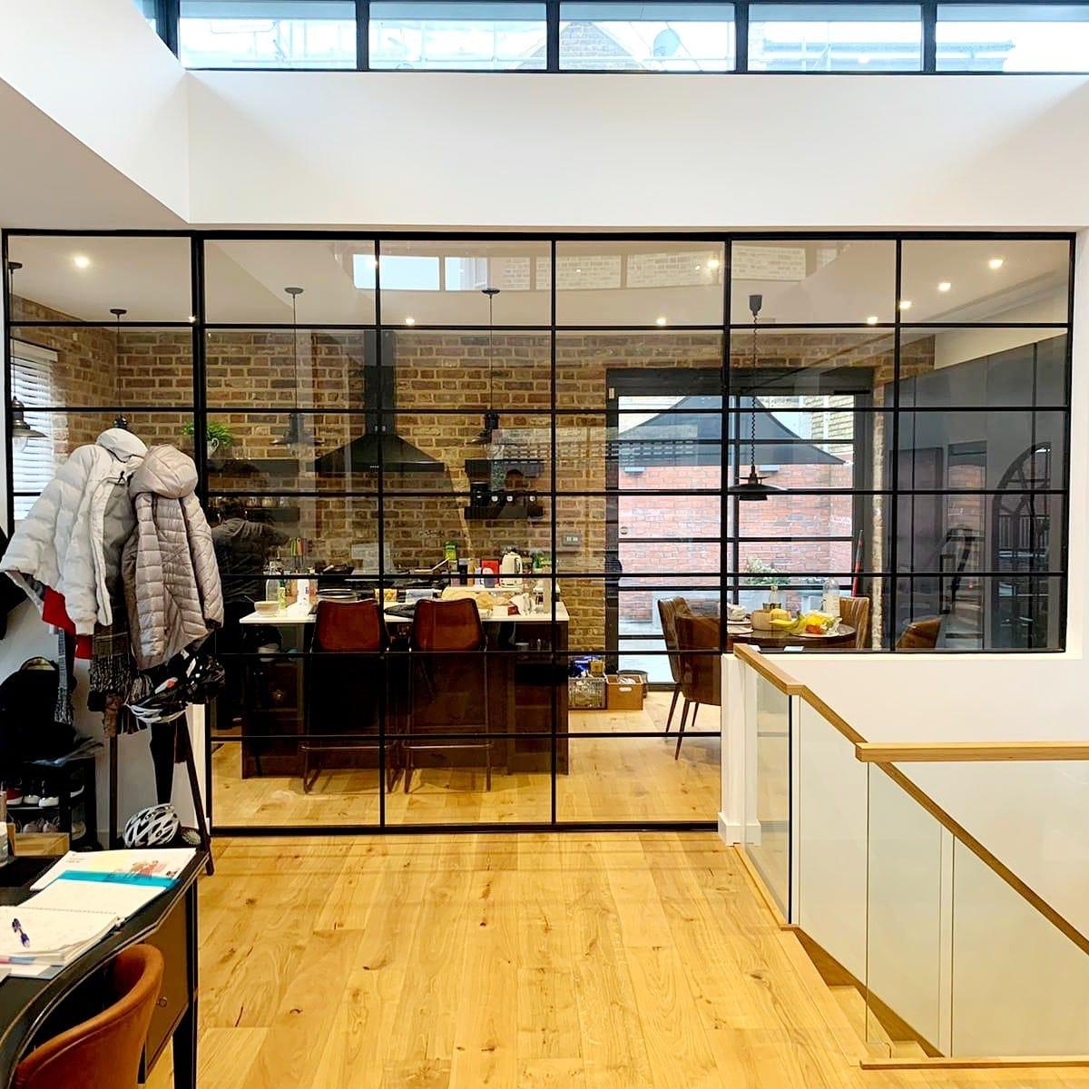 Double-height space with black glazed screens over a brick-walled kitchen