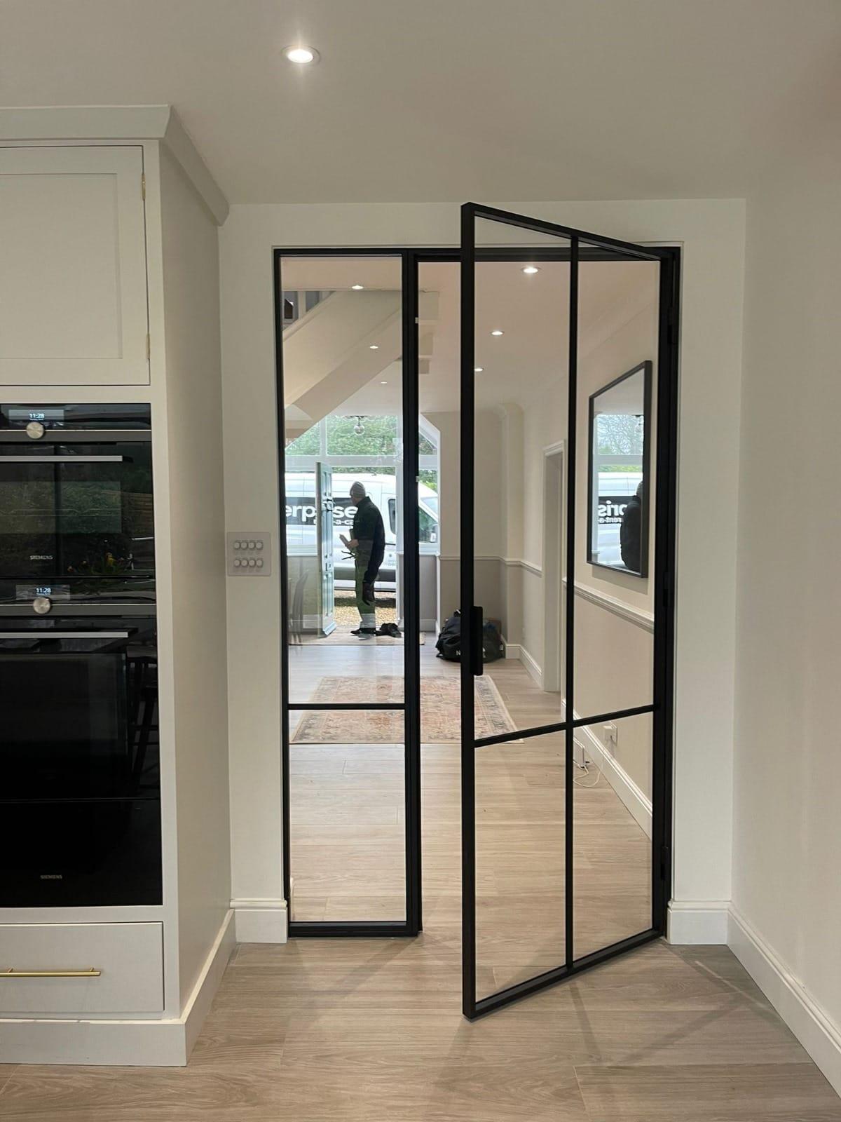Black steel glazed door off a kitchen, the hallway visible through it