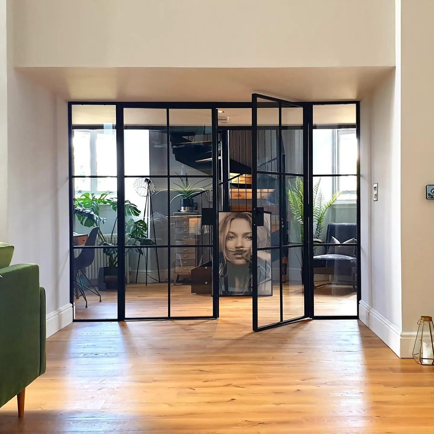 Black steel pivot doors standing open between two reception rooms, over an oak floor