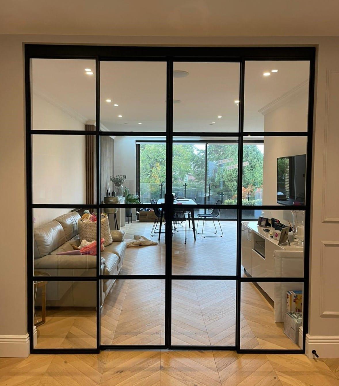 Black Crittall-style screen dividing a living room from the kitchen and garden doors beyond