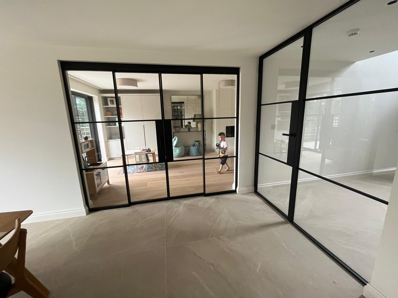 Black steel glazed screens returning around a corner in an open-plan ground floor