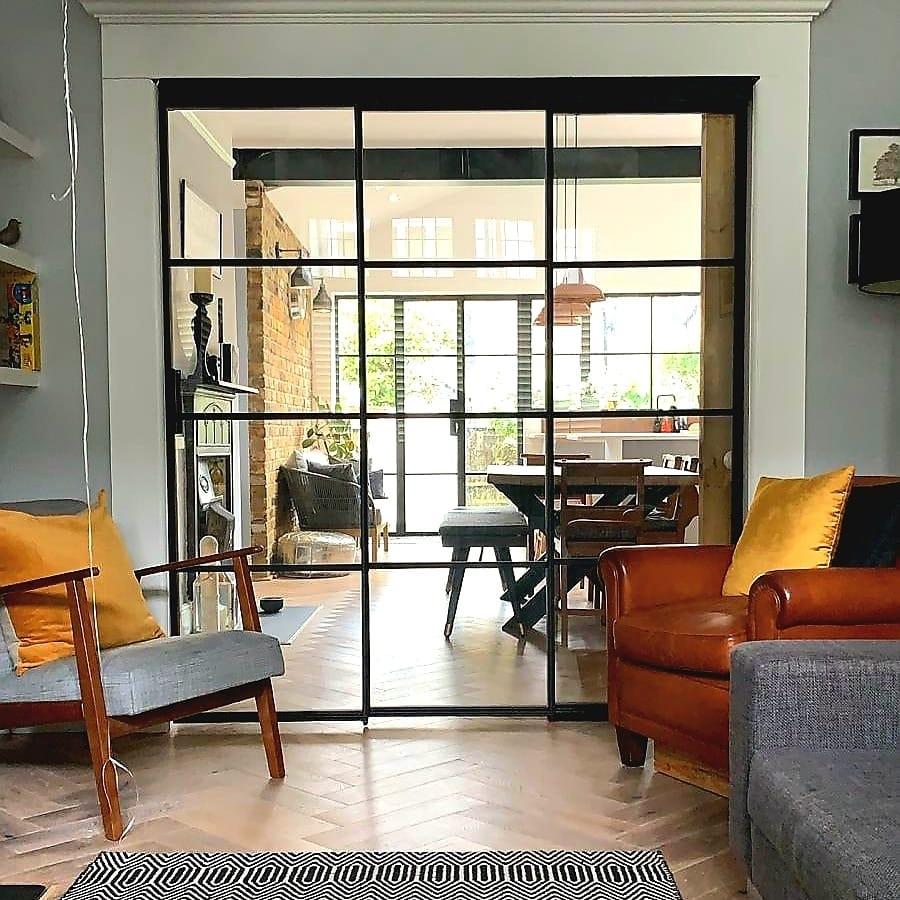 Black Crittall-style screen from a living room into a brick-walled kitchen under a rooflight