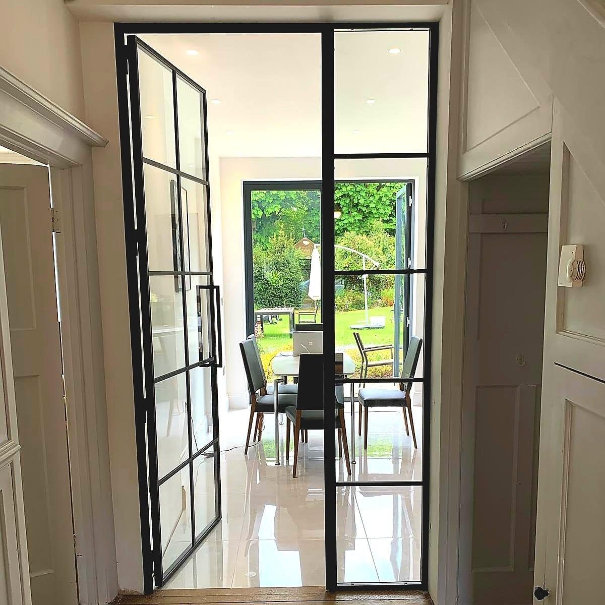 Black steel French doors opening onto a garden terrace, the dining area beyond
