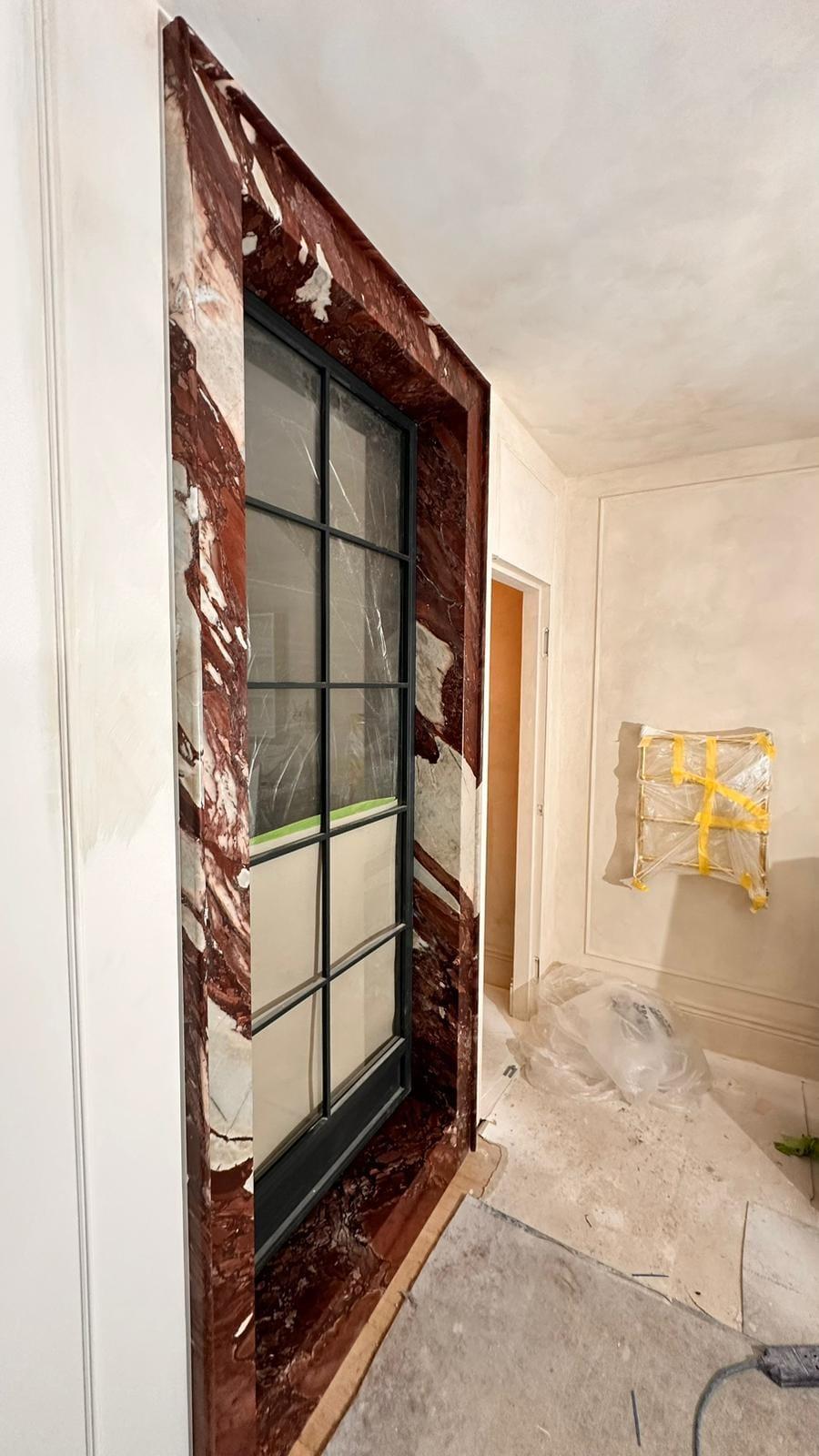 Rosso marble door surround being set around a black steel glazed door, the room still in plaster