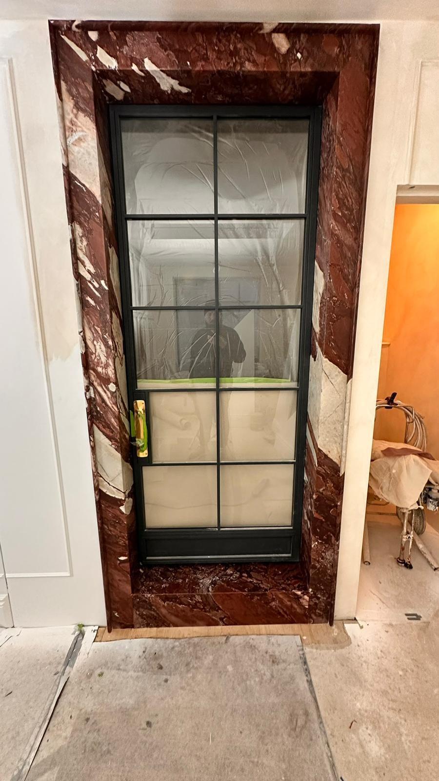 Rosso marble surround framing a black steel glazed door, protective tape still on the ironmongery