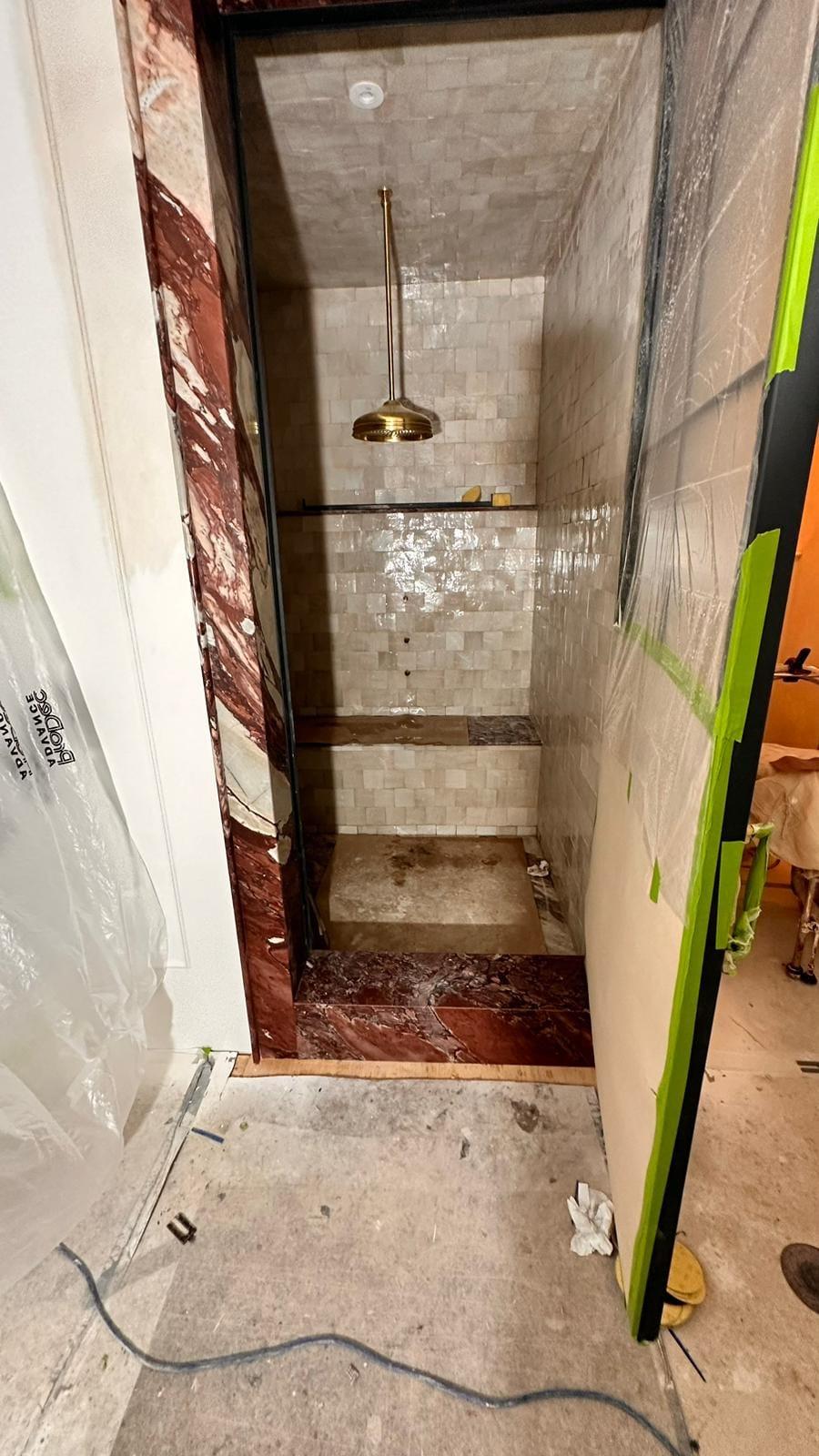 Shower enclosure in a rosso marble surround, mid-install with the glass still protected