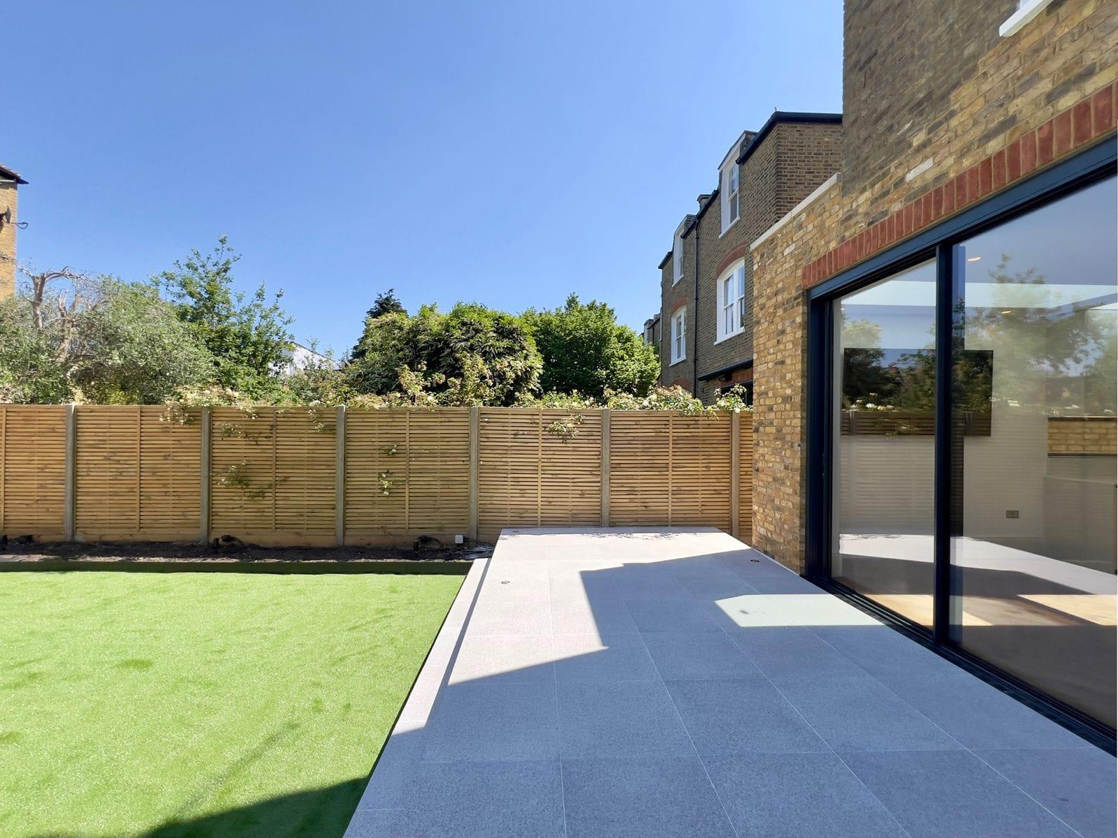 Rear garden after landscaping — porcelain paving, artificial lawn and full-height sliding doors
