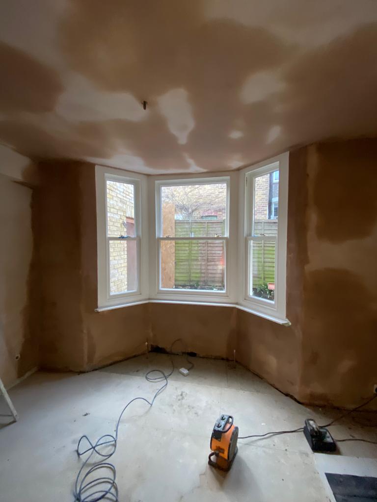 A London room stripped back to fresh plaster mid-renovation, sheeted floor and tools still on the boards — the state a stalled build is usually left in