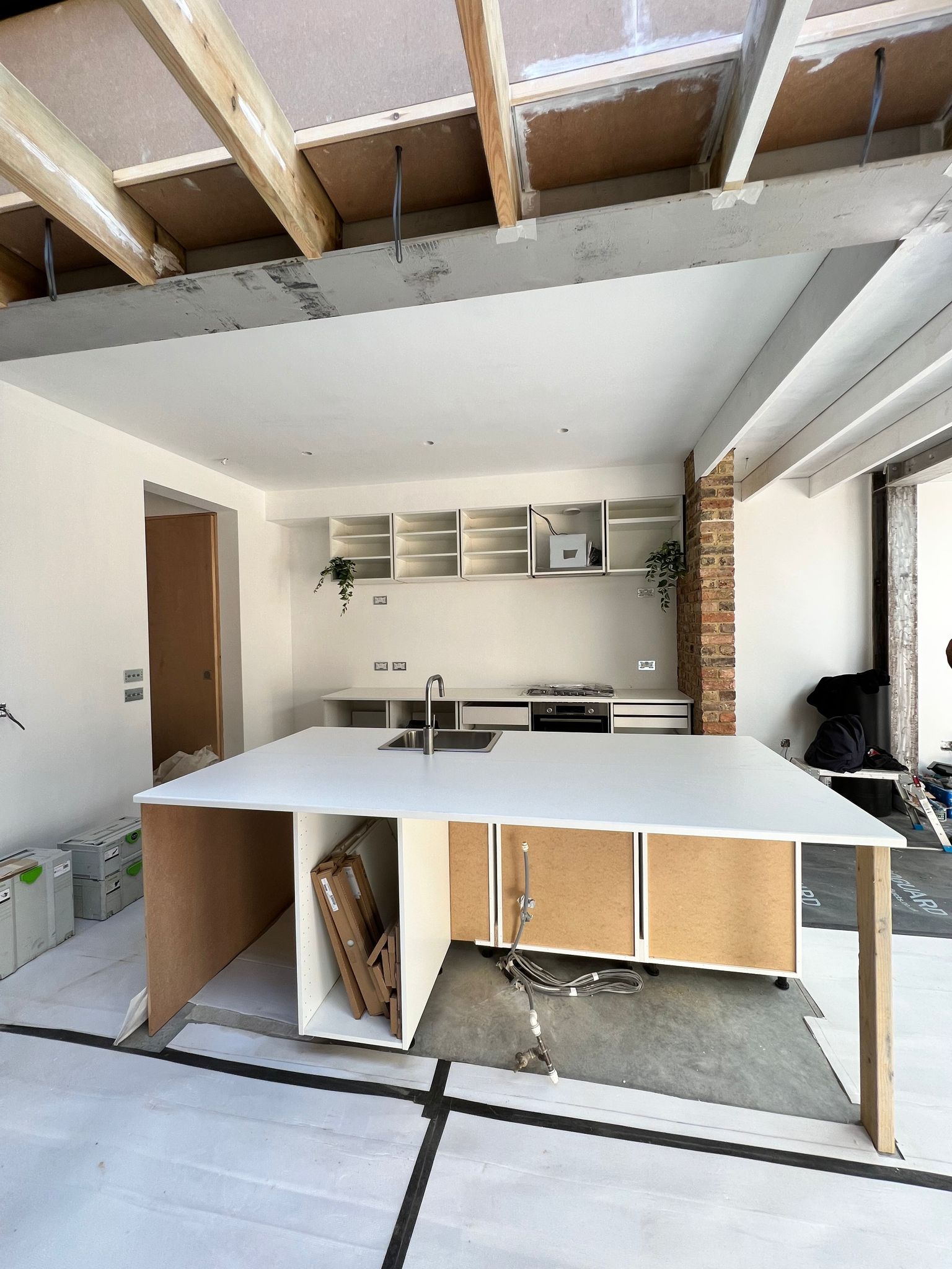 Our own carcasses going in — Island built and levelled, worktop set, doors stacked ready to hang under an open rooflight