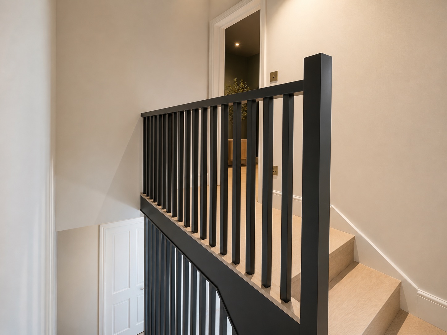 Finished staircase with a slim black square-section balustrade and newel post, pale oak treads and landing